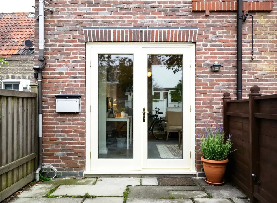 Gebroken wit geschilderde houten openslaande tuindeuren met elk één grote ruit, onder een rollaag in een bakstenen achtergevel